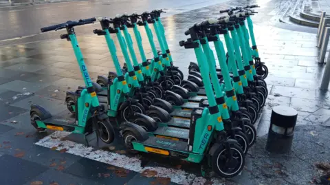 Owen Ward/BBC Green Tier branded electric scooters parked in Chelmsford city centre.