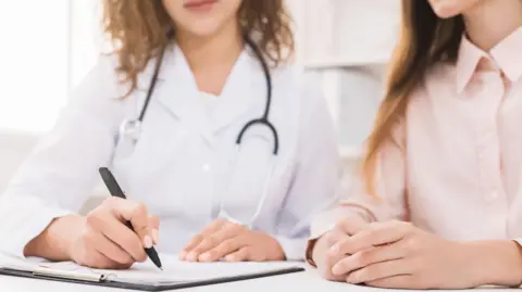 Getty Images Médico escrevendo notas sobre um jovem paciente