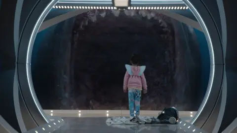 Courtesy of Warner Bros. A small child stands in front of a large shark with its jaws open