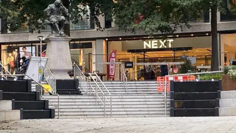 Local Democracy Reporting Service A statue and stone and black metal steps in Hay Hill in front of Next