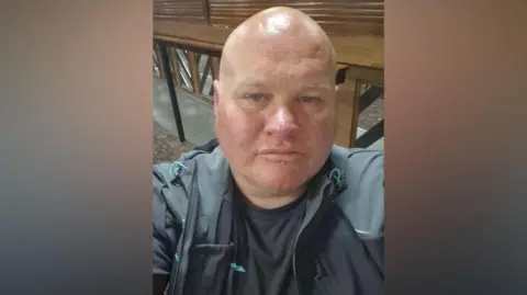 Paul Clarke A selfie of a man wearing a dark jacket, with wooden panels and seating behind.

