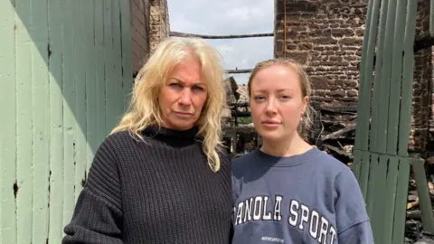A woman with blond hair and wearing a black jumper hugging another woman with a scraped-back hairstyle and a blue sweatshirt with white lettering.