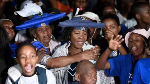 Getty Images Multiple supporters of the UDC party stand at a rally donning white and blue.