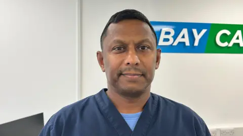 A man from Sri Lanka wearing a blue carers uniform