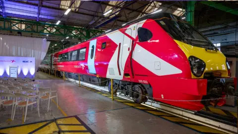 An image of the newly refurbished CrossCountry Voyager train inside a warehouse at the launch event. The train has bright shiny red paint with a white X on the driver's door.