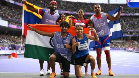 Getty Images Simran and Abhay kneeling, holding the Indian flag behind them, having come third in the 200m in Paris. Behind them are the pairs who came first and second with their national flags. 