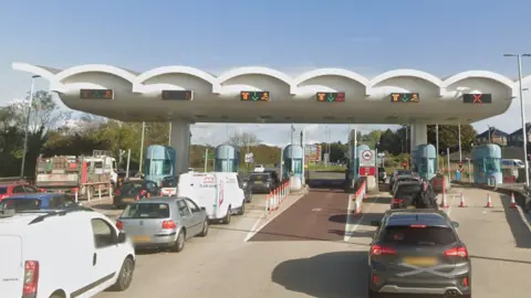 A queue of vehicles waiting to go through a series of toll lanes on a bridge.