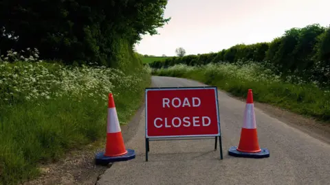 Getty Images Road closed sign alongside some traffic cones on a country road