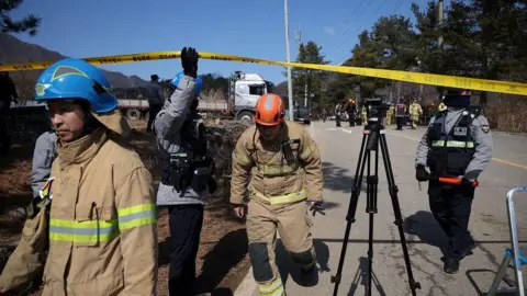 Reuters Firefighters and security personnel crossing under a yellow police tape cordoning off the bomb site