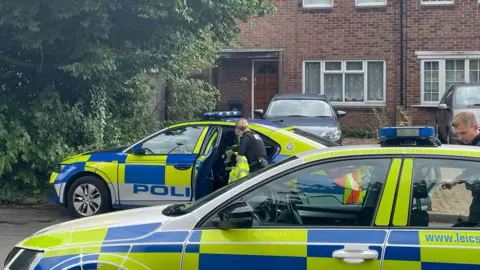 Matthew Cooper/PA Wire Police officers and two police cars outside a house in Hopyard Close in Leicester