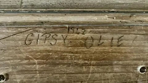 Kit Taylor/BBC A wooden fireplace with the names Gipsy and Olie and the year 1942 carved in. 