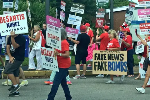 Morgan Finkelstein Protester with placard reading "Fake News Fame Bombs"