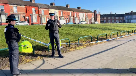 Two police officers talk on the pavement in front of a police cordon 