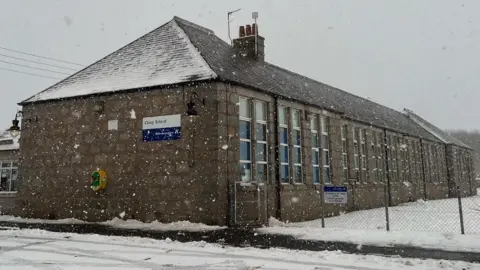 Snow is falling in this chilly scene at Cluny School. The school is building is of a Victorian design. There is snow on the ground around it.