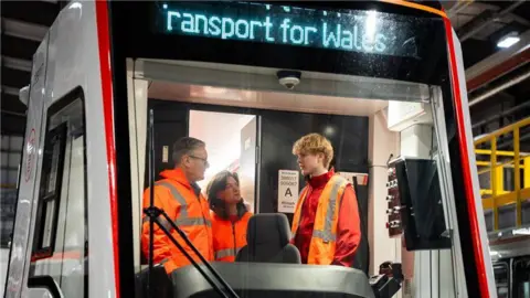 Welsh Government Keir Starmer, Eluned Morgan and a train worker stood in the cab of a TFW tram-train vehicle.