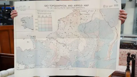 Jacob King/PA Wire A map showing the coast of Normandy being held up. It has colour codes and black dots to show areas of sites for rapid airfield construction