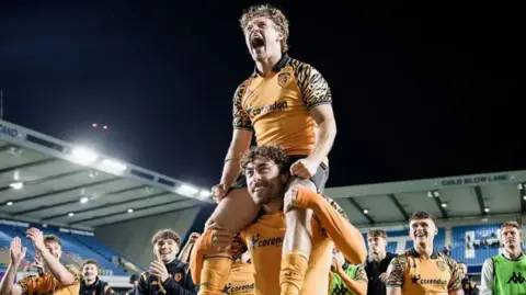 Getty Images One Hull City footballer sits on top of another player's shoulders in celebration of their team's victory.