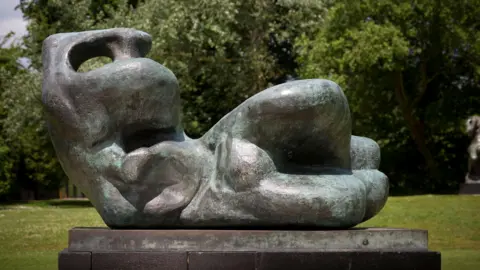 Jonty Wilde Abstract reclining bronze figure by Henry Moore displayed outdoors on a plinth with trees in the background