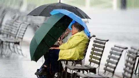 PA Media A racegoer shelters from the rain on the first day of the Cambridgeshire Meeting at Newmarket Racecourse.