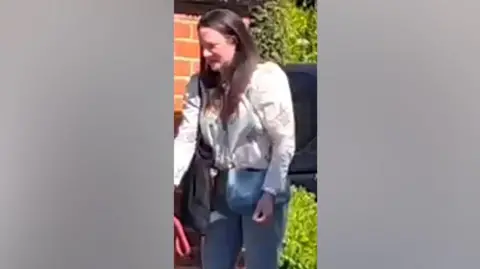 Claire Freemantle outside a building, wearing a white top, jeans and over-the-shoulder bag