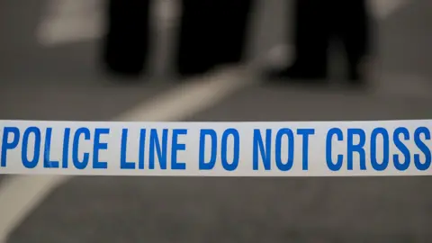 Stock image of police tape which says "Do not cross" in blue on white tape. The background is blurry.