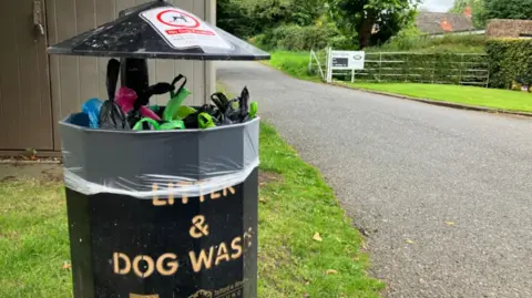 A bin full of dog poo bags in a park.