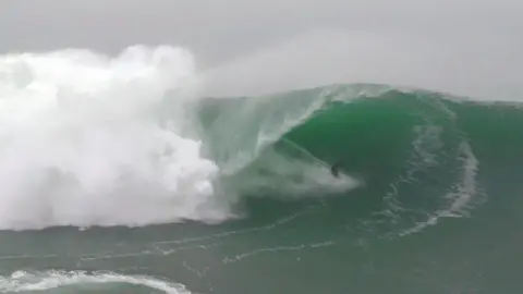 A wide shot of a surfer riding the tube of a large wave as it curls and breaks 