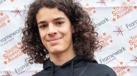 Isa, with shoulder-length curly brown hair, smiling in front of Framework branding