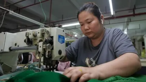 Sofa factory worker sits in front of a sewing machine in Foshan