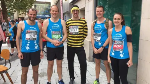 Four runners with a man in the middle wearing yellow and black stripes