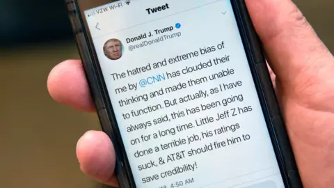 Getty Images A man holds up his phone displaying a tweet by US President Donald Trump attacking CNN