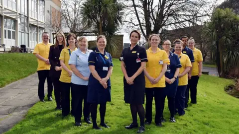 Somerset NHS Foundation Trust Somerset NHS Foundation Trust's specialist dementia and delirium team - 10 nurses wearing yellow and blue are standing outside smiling into the camera