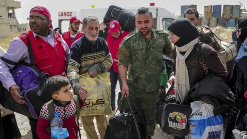 EPA Handout photo shows Syrian soldiers and Syrian Arab Red Crescent employees (SARC) assisting civilians leaving the rebel-held town of Douma, in the Eastern Ghouta (27 March 2018)