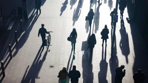 Getty Images Se ven siluetas de personas mientras caminan sobre una acera bien iluminada.