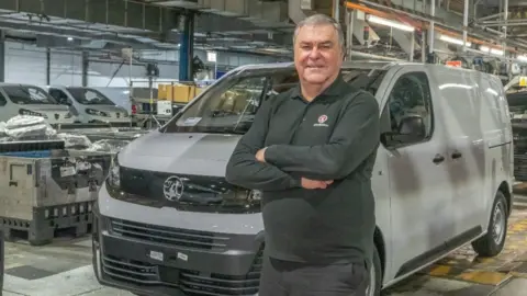 Mark Noble in the factory standing in front of a van