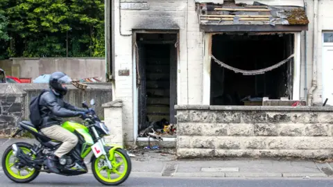 A motorist drives his motorcycle past a damaged house, after a second night of an anti-immigration demonstration in Ballymena, Northern Ireland, on June 11, 2025.