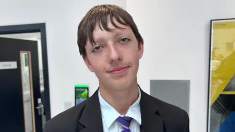 Kate Bradbrook/BBC A boy in a school uniform with a purple, white and black coloured tie.