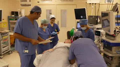 Pinky Jolley on a surgery table surrounded by medical professionals in blue scrubs and masks