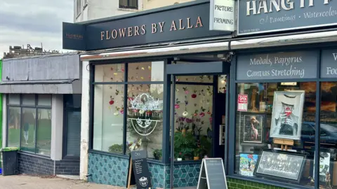 There are individual flowers hanging in a window display at the Flowers By Alla store. 