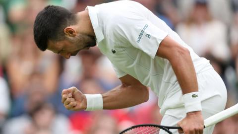 Novak Djokovic bends over, clenches his fist and roars in celebration during his Wimbledon first-round match against Vit Kopriva