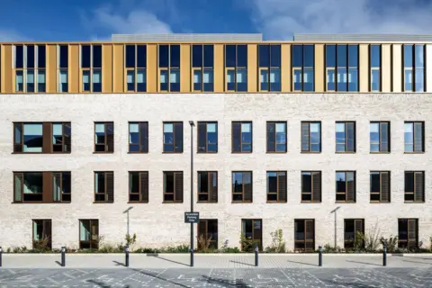 Keith Hunter The exterior of a bright building with many rectangular windows.