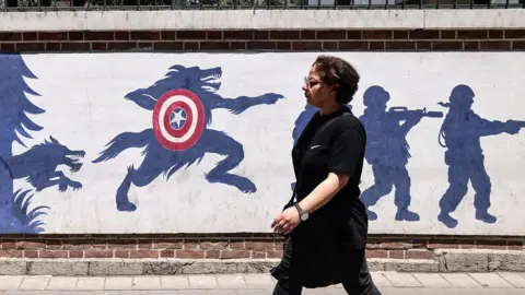A woman wearing a black dress walks past an anti-US mural outside the former US embassy in Tehran on 15 June. 