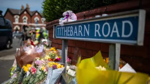 PA Media Bouquets of flowers underneath a street sign for Tithebarn Road. A light purple unicorn toy sits on top of the street sign.