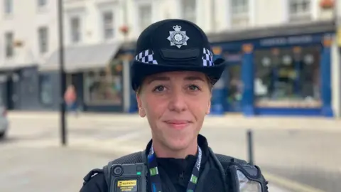 Laura Coffey/BBC A female police office stood on a street with shops behind her. She is looking at the camera and smiling.