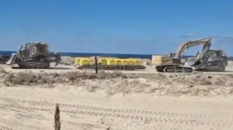 Reuters via IDF Two excavators are pictured on either side of a set of yellow blocks on sandy ground in Gaza