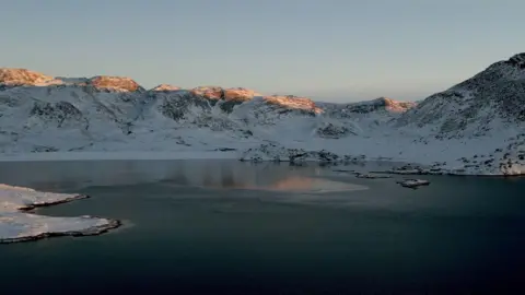 BBC drone photo of a fjord with snow-capped mountains in the background