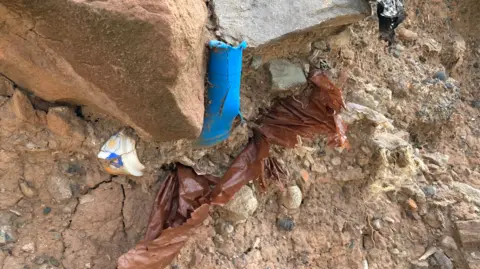 Plastic tubing and other items poke through soil and rock.