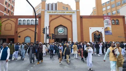 Getty Images The East London Mosque, a modern red brick building. A large number of males in Islamic dress appear to be walking away from it towards the camera.