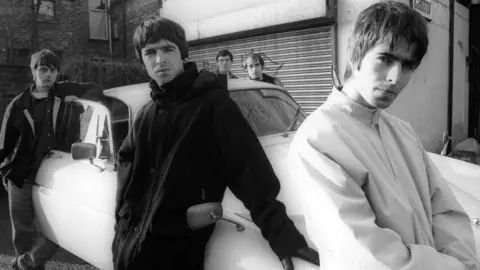 Getty Images The original line-up of Oasis stand around a white Jaguar car in front of a shutter-fronted shop in a black and white photograph