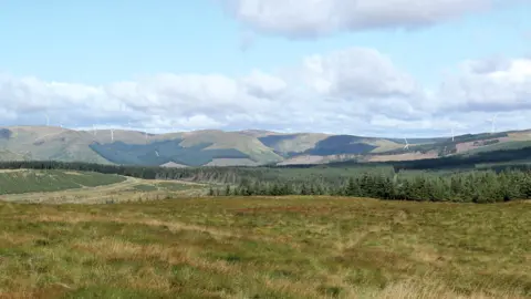 A view of rolling hills in the south of Scotland with some wind turbines dotted along them